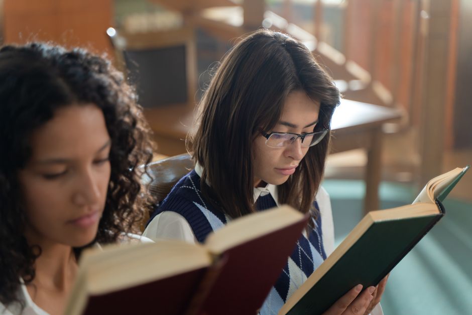Two female students reading books in an educational setting. Perfect for school and study themes.